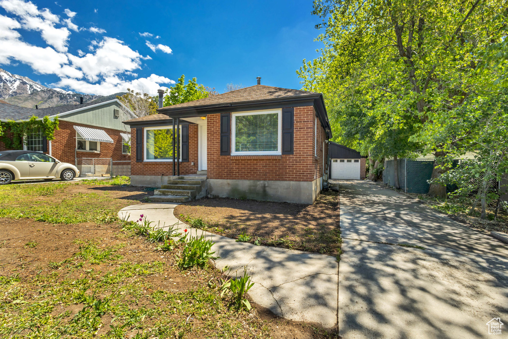View of front of property featuring brick siding, fence, an outdoor structure, a garage, and concrete driveway