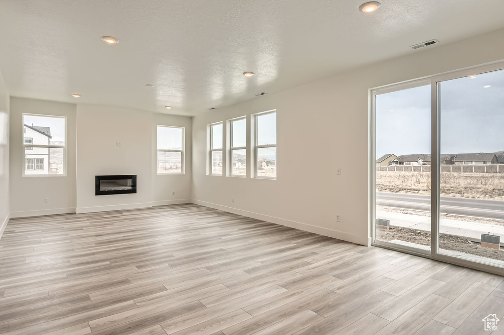 Unfurnished living room featuring light wood-style floors, baseboards, a glass covered fireplace, and recessed lighting