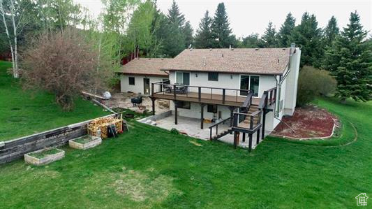 Back of property featuring a wooden deck, a patio, a chimney, and a lawn