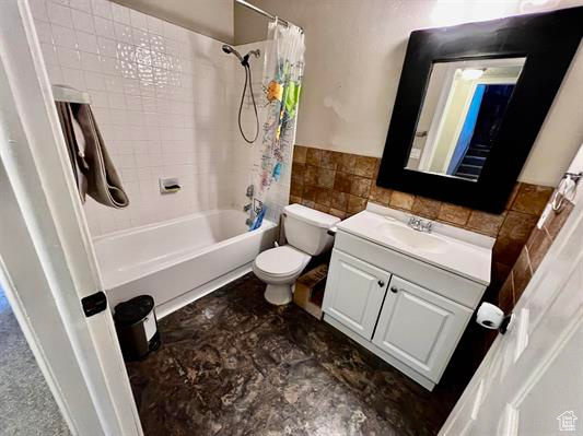 Bathroom with tile walls, toilet, shower / bath combination with curtain, vanity, and a wainscoted wall