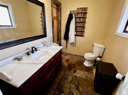 Bathroom featuring stone tile flooring, vanity, healthy amount of natural light, and toilet