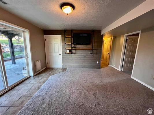 Unfurnished living room featuring a textured ceiling, wooden walls, baseboards, and light tile patterned floors