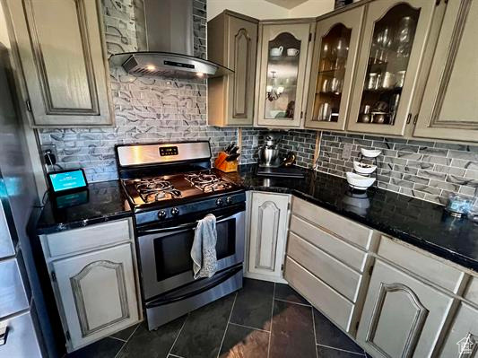 Kitchen featuring appliances with stainless steel finishes, wall chimney exhaust hood, dark tile patterned flooring, decorative backsplash, and glass insert cabinets