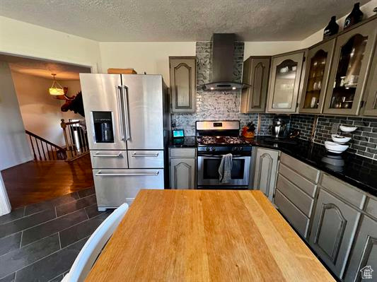 Kitchen with appliances with stainless steel finishes, wall chimney exhaust hood, backsplash, glass insert cabinets, and a textured ceiling