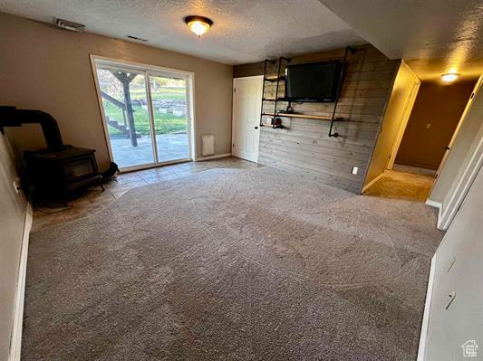 Unfurnished living room featuring a wood stove, a textured ceiling, carpet, and baseboards