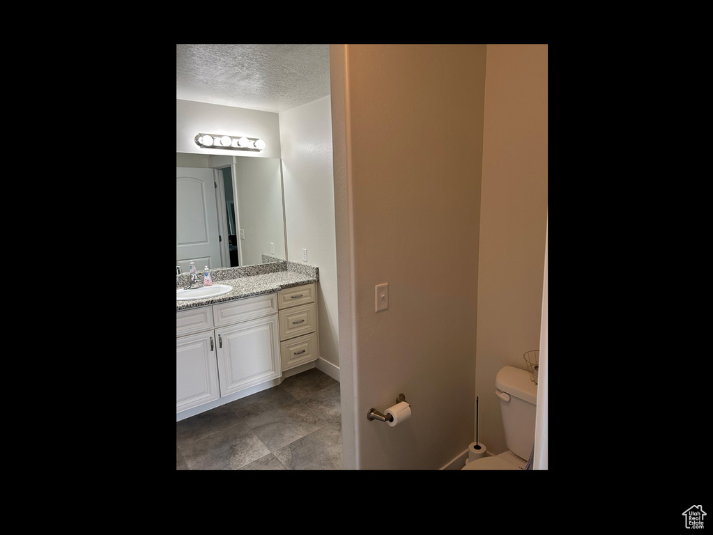 Half bathroom with a textured ceiling, toilet, vanity, tile patterned flooring, and baseboards