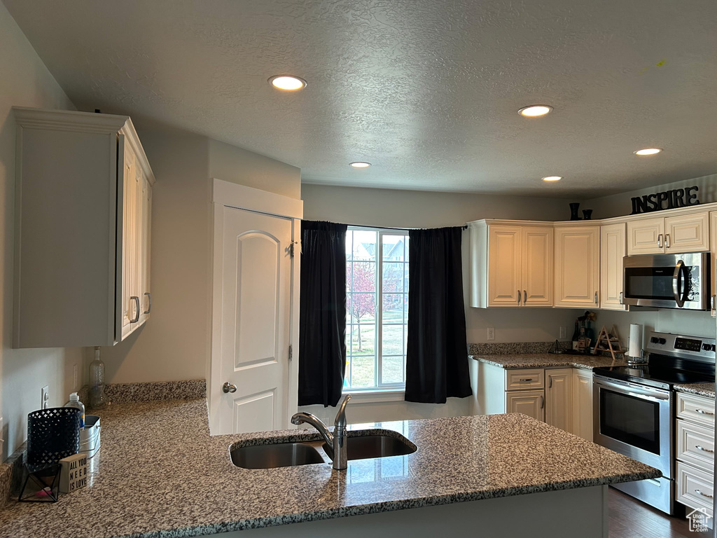 Kitchen featuring stainless steel appliances, a sink, recessed lighting, stone countertops, and a textured ceiling