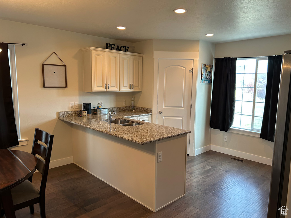 Kitchen featuring a sink, baseboards, light stone counters, dark wood-type flooring, and recessed lighting