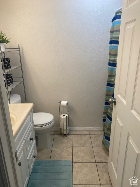 Bathroom with toilet, vanity, tile patterned floors, baseboards, and curtained shower
