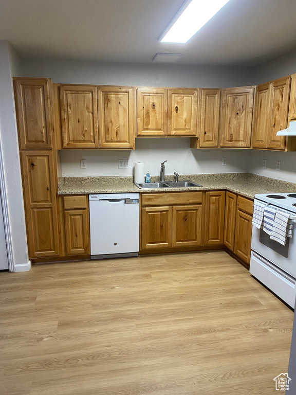 Kitchen with white appliances, a sink, under cabinet range hood, and light wood finished floors