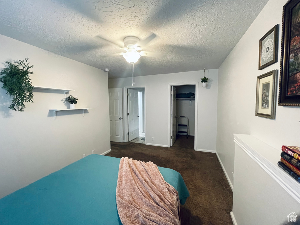 Carpeted bedroom featuring a textured ceiling, baseboards, a ceiling fan, a walk in closet, and a closet