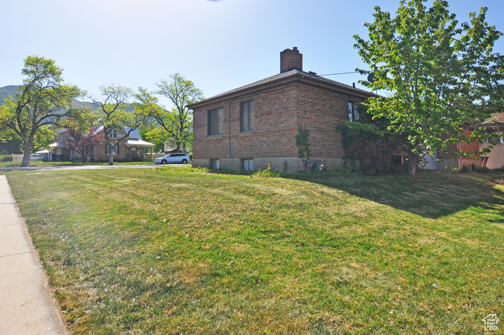 View of side of home with a chimney, brick siding, and a lawn