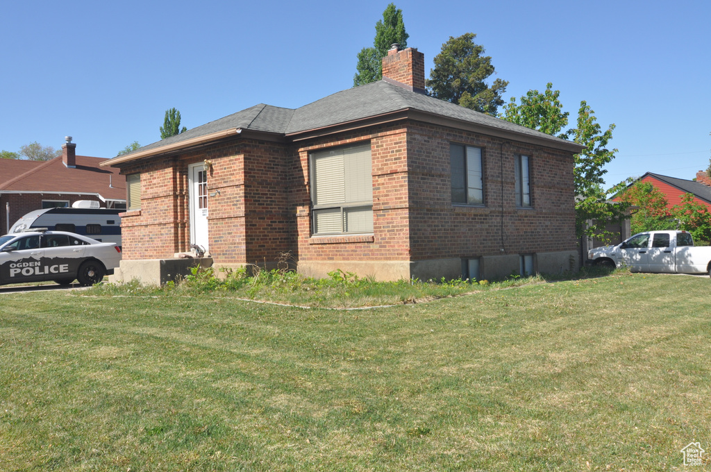 View of property exterior featuring brick siding, a yard, and a chimney