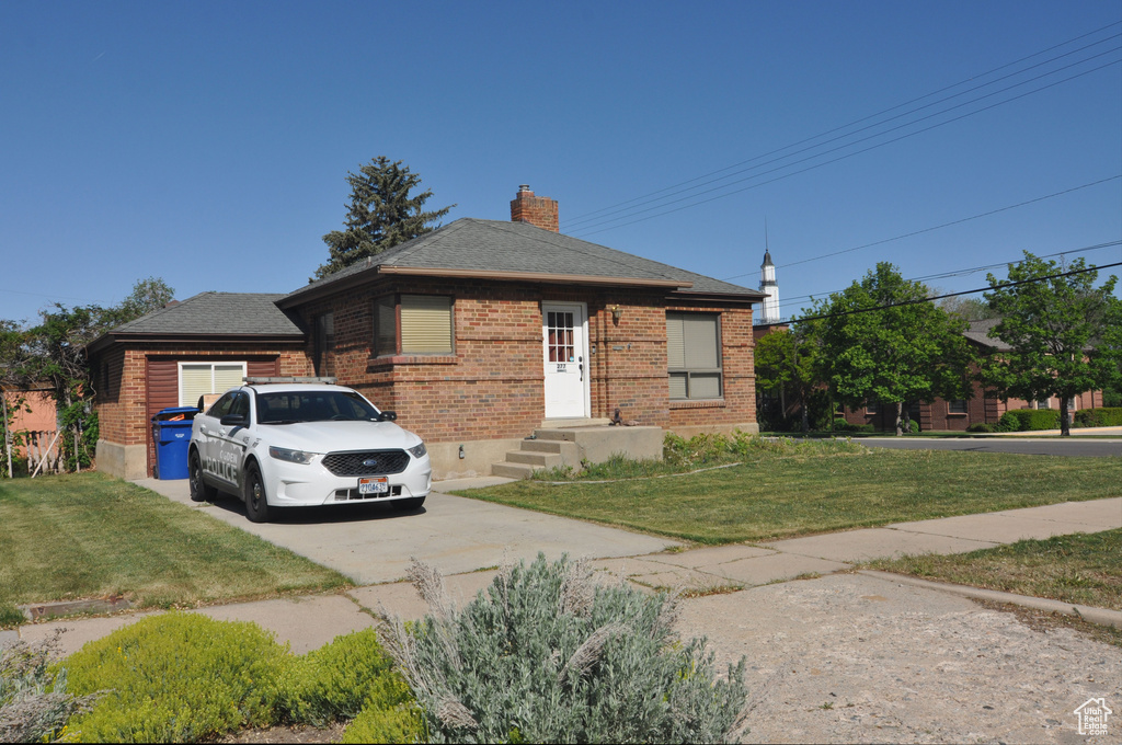 Bungalow-style home with brick siding, concrete driveway, a front yard, and a chimney