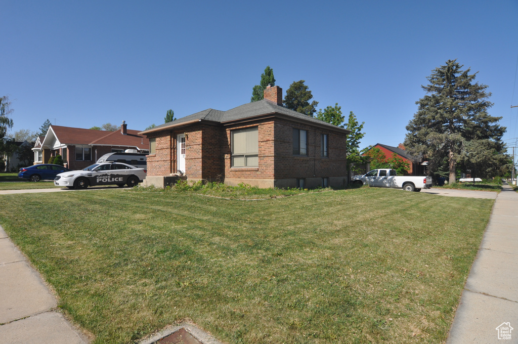 View of side of property featuring brick siding, a yard, and a chimney