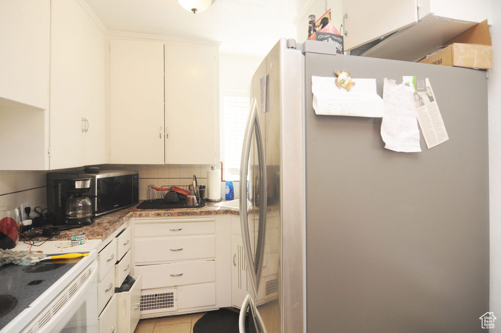 Kitchen featuring freestanding refrigerator, decorative backsplash, white cabinets, and light tile patterned flooring