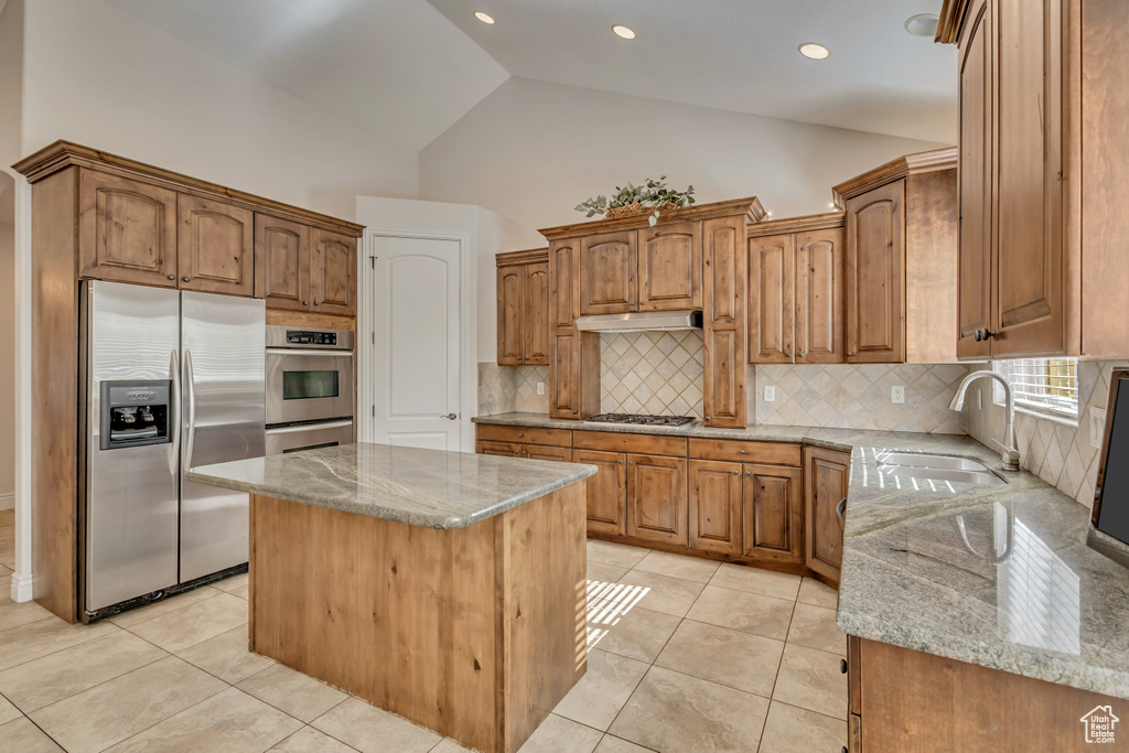 Kitchen with stainless steel appliances, light stone counters, a sink, tasteful backsplash, and high vaulted ceiling