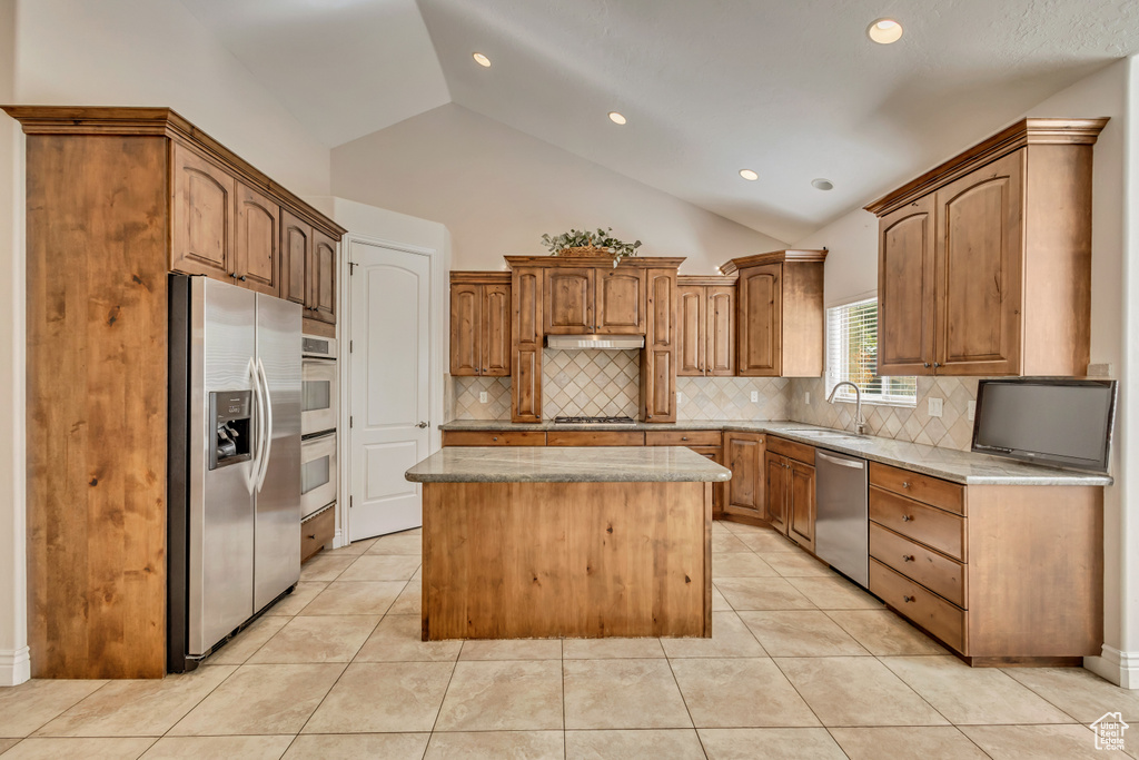 Kitchen featuring stainless steel appliances, a sink, a center island, tasteful backsplash, and light stone countertops