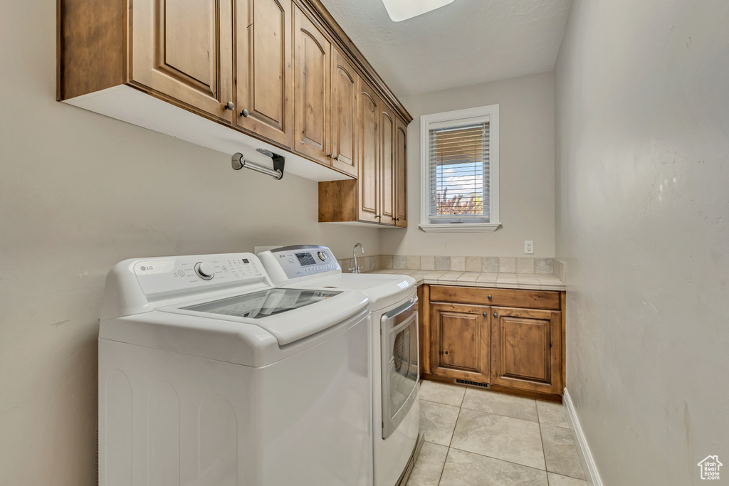 Laundry area with cabinet space, washer and clothes dryer, light tile patterned flooring, and baseboards