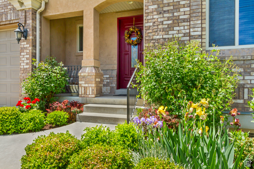 Doorway to property with covered porch, stone siding, stucco siding, and a garage