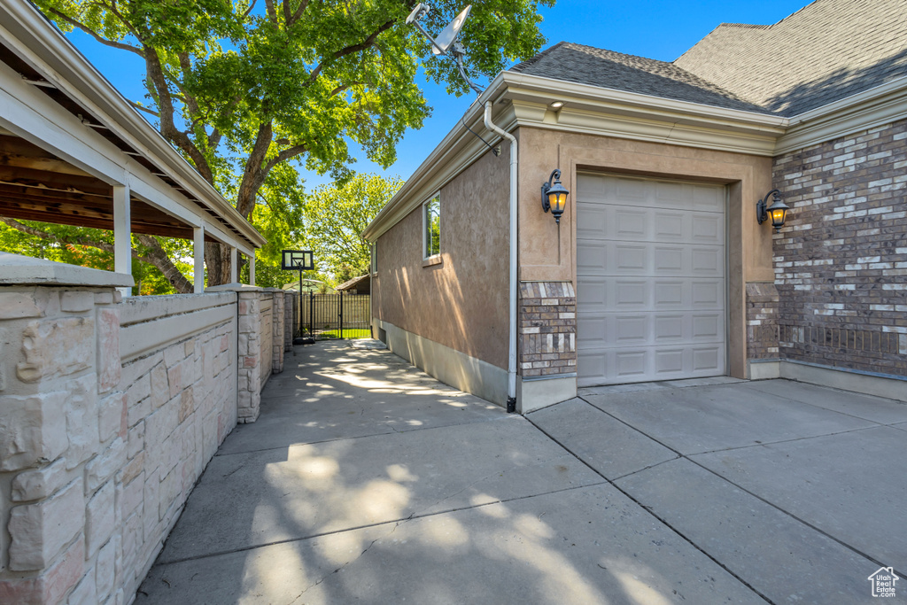View of side of property with an attached garage, concrete driveway, fence, roof with shingles, and stucco siding