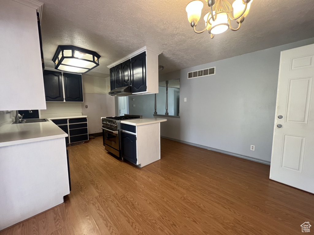 Kitchen with gas range, a chandelier, a sink, light countertops, and a textured ceiling