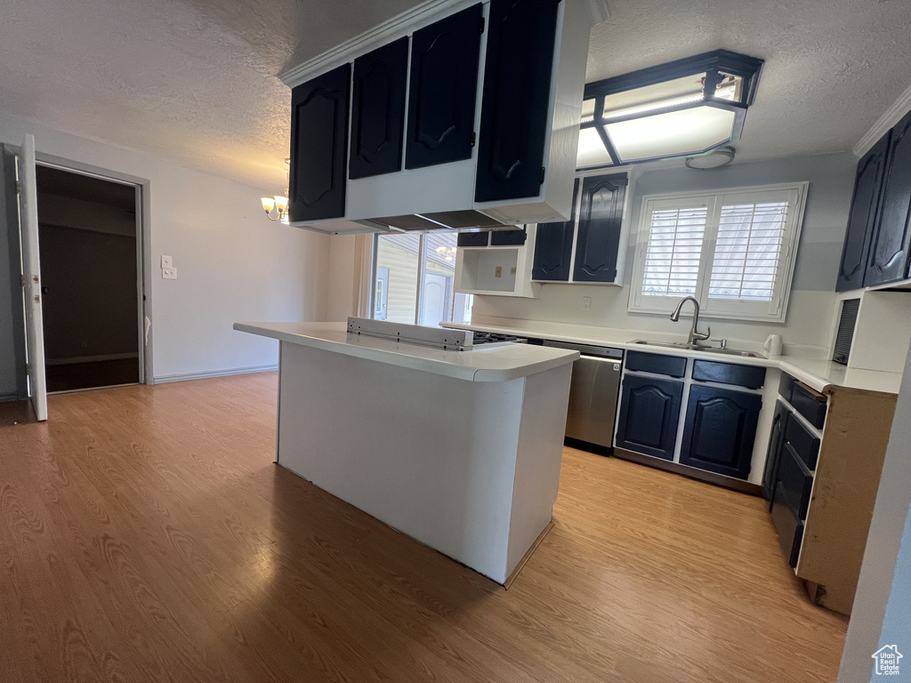 Kitchen with a textured ceiling, a sink, light countertops, light wood-style floors, and stainless steel dishwasher