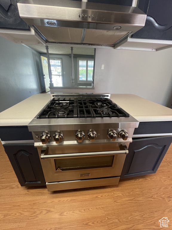 Kitchen with under cabinet range hood, light countertops, high end stainless steel range oven, and light wood-type flooring