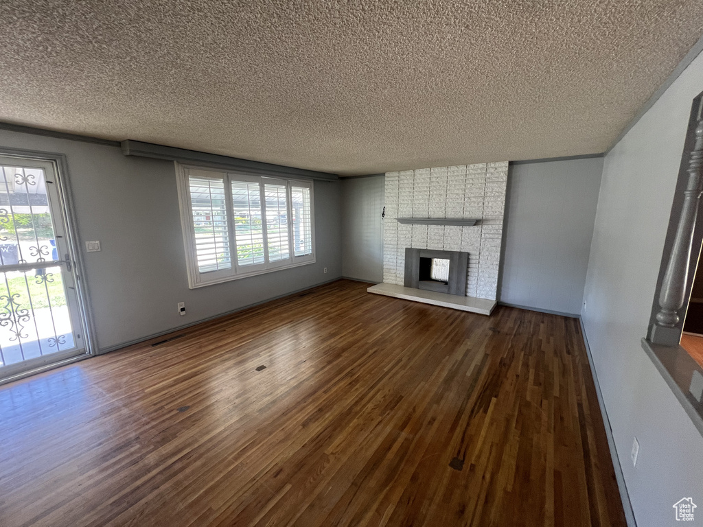 Unfurnished living room featuring a textured ceiling, dark wood-style flooring, plenty of natural light, a brick fireplace, and baseboards