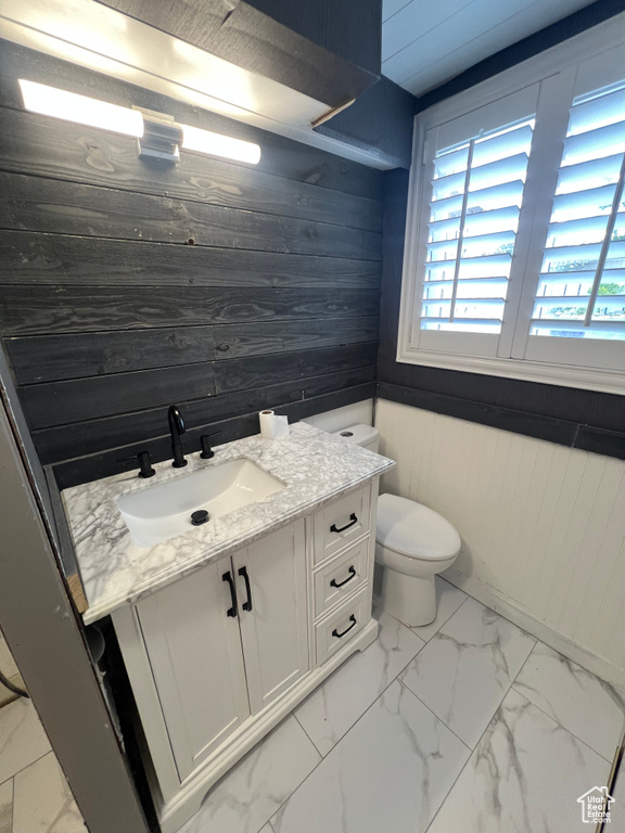 Bathroom with wood walls, marble finish floors, vanity, and toilet