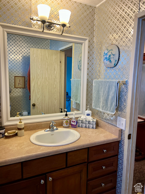 Bathroom with vanity, a chandelier, and wallpapered walls
