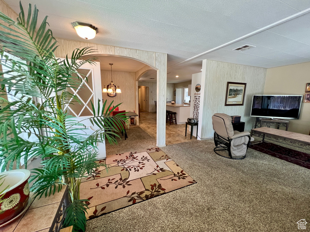 Living area featuring arched walkways, carpet floors, a chandelier, and wood walls