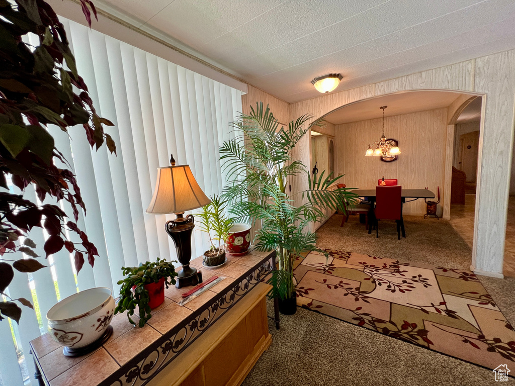 Hallway with arched walkways, carpet, a chandelier, and wooden walls