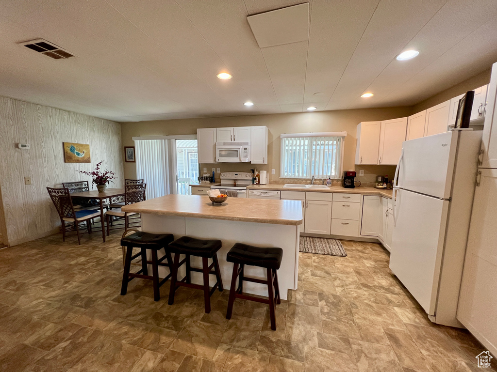 Kitchen with white appliances, a sink, a kitchen island, a kitchen breakfast bar, and white cabinetry