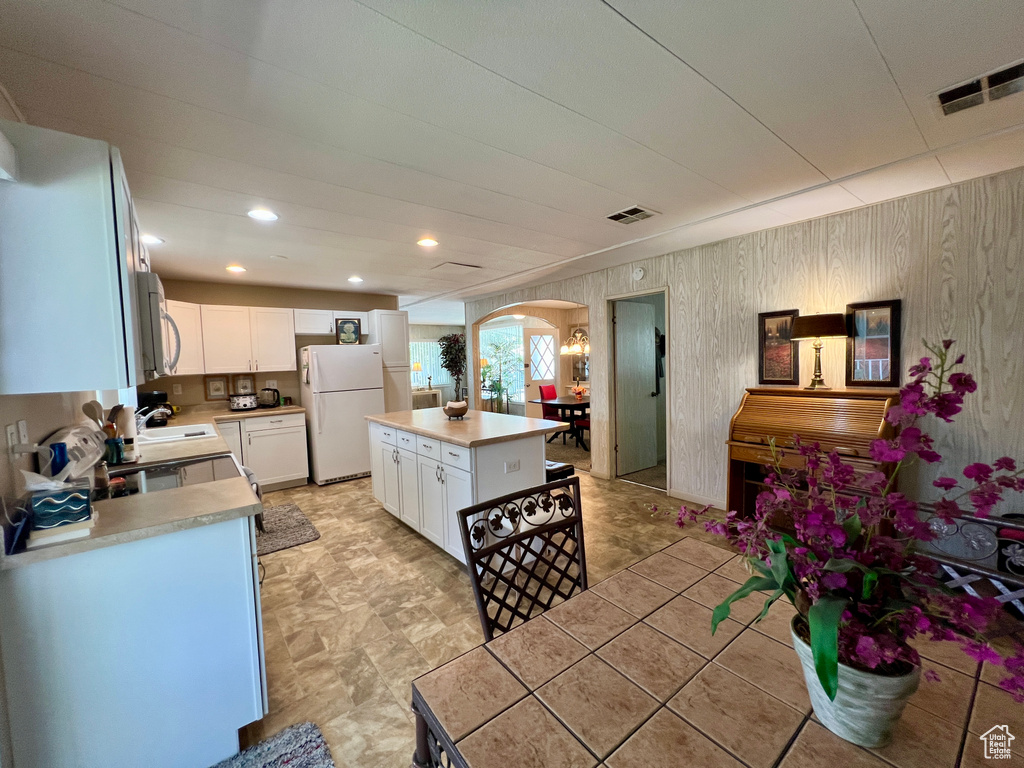 Kitchen featuring white appliances, arched walkways, light countertops, white cabinetry, and wooden walls