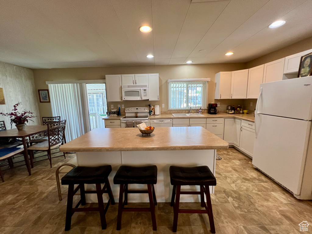 Kitchen featuring white appliances, a kitchen breakfast bar, a center island, light countertops, and white cabinetry