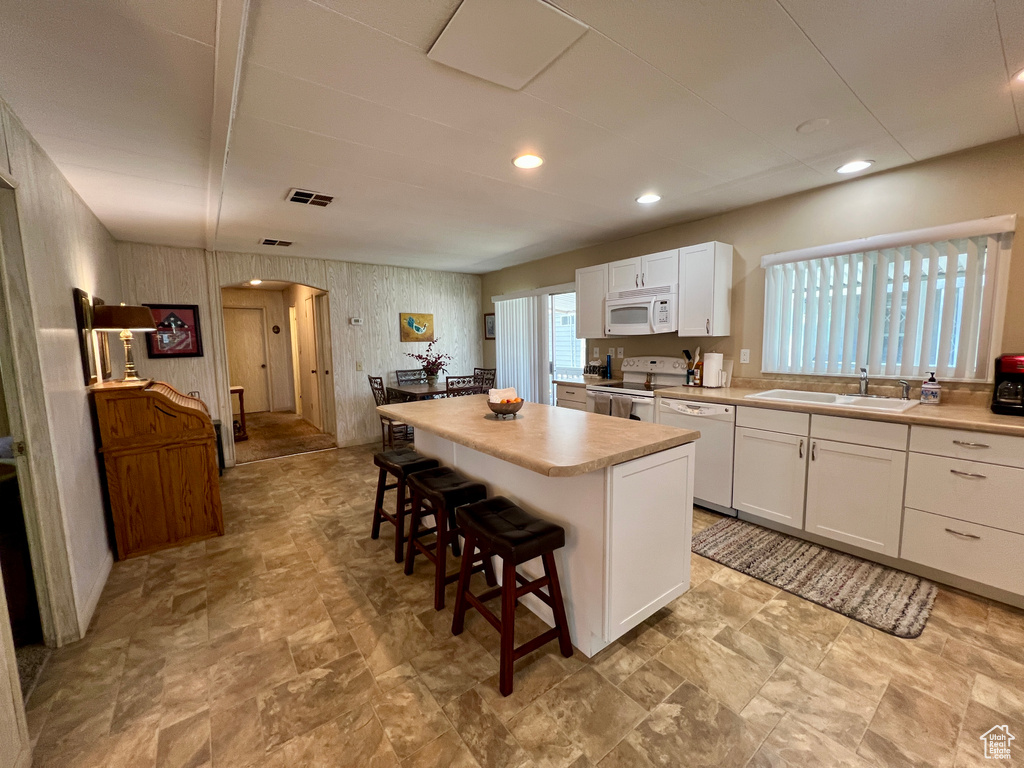 Kitchen featuring white appliances, a sink, arched walkways, a kitchen island, and a kitchen breakfast bar