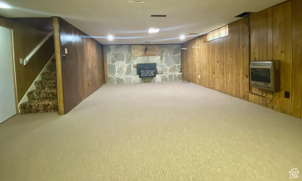 Finished below grade area featuring wood walls, heating unit, stairway, carpet, and a stone fireplace