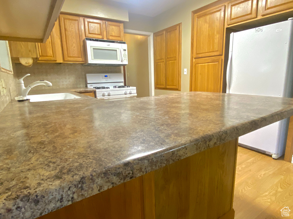 Kitchen with white appliances, a sink, a peninsula, brown cabinetry, and dark countertops