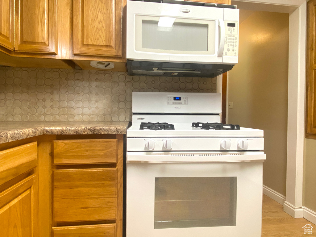 Kitchen featuring white appliances, backsplash, light countertops, light wood-style flooring, and baseboards