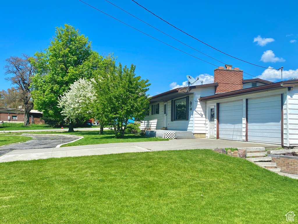 View of front of house featuring a front yard, a chimney, driveway, and a garage