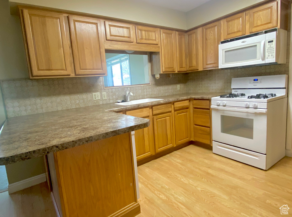 Kitchen with white appliances, a sink, a peninsula, light wood-type flooring, and decorative backsplash