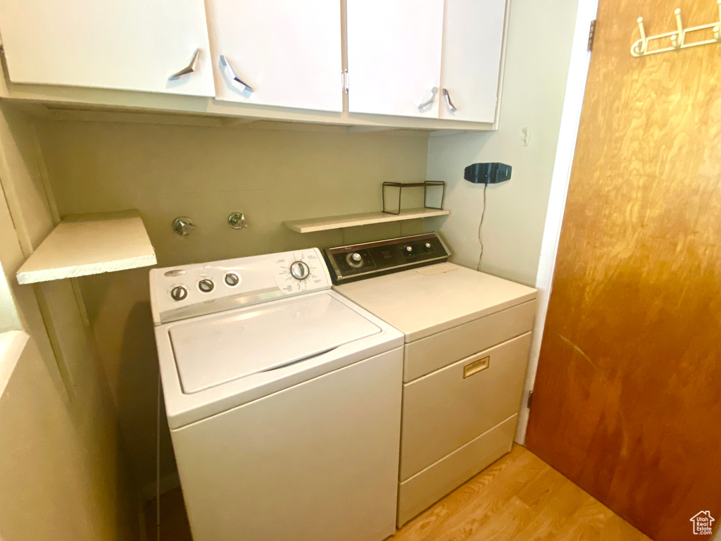 Washroom with separate washer and dryer, cabinet space, and light wood-style floors