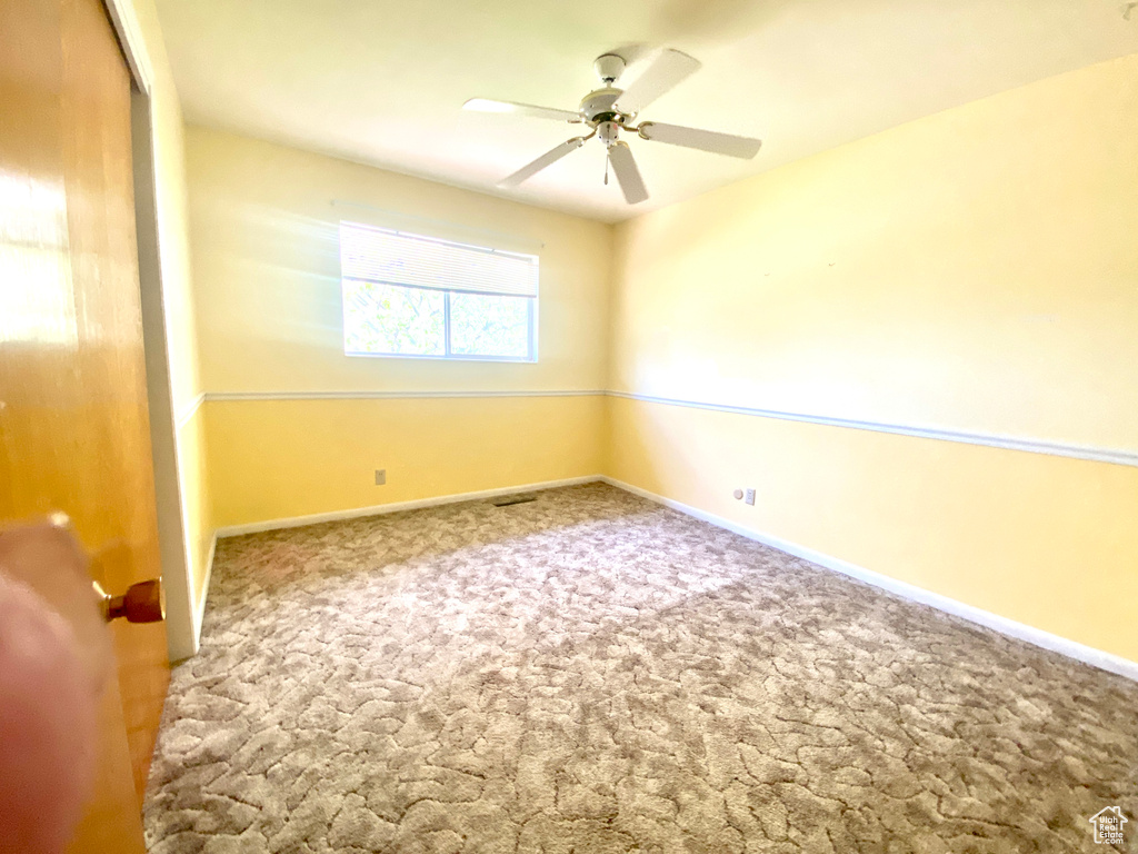 Carpeted empty room featuring ceiling fan and baseboards