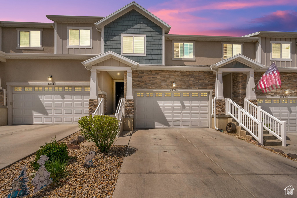 Townhome / multi-family property featuring concrete driveway, an attached garage, board and batten siding, and stone siding
