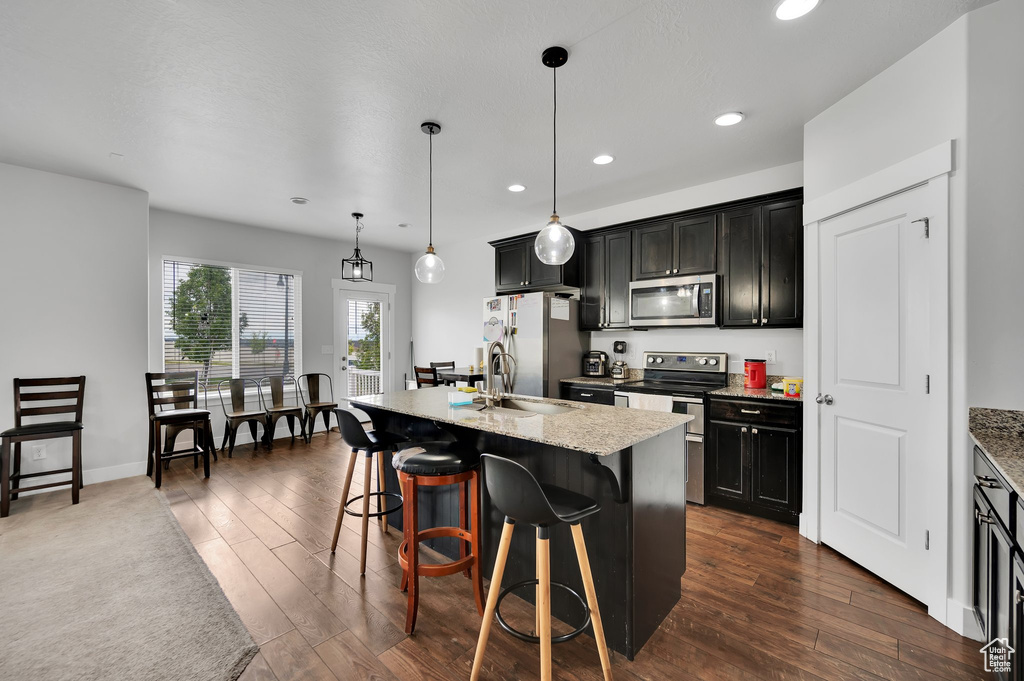 Kitchen with a sink, appliances with stainless steel finishes, dark wood-style floors, and a breakfast bar