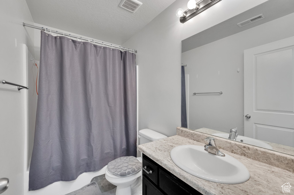 Full bathroom featuring vanity, toilet, a textured ceiling, and visible vents