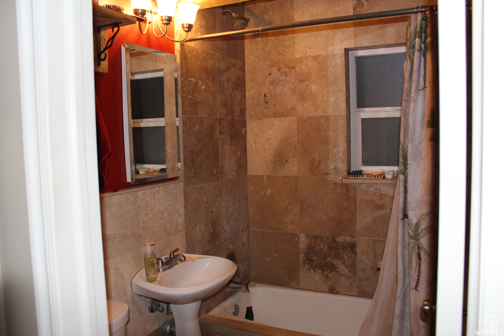 Full bathroom featuring a chandelier, toilet, shower / bath combination with curtain, tile walls, and a sink