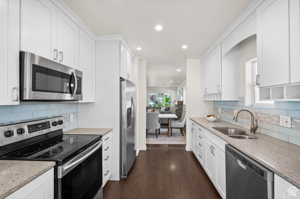 Kitchen with appliances with stainless steel finishes, a sink, recessed lighting, white cabinetry, and dark wood-type flooring