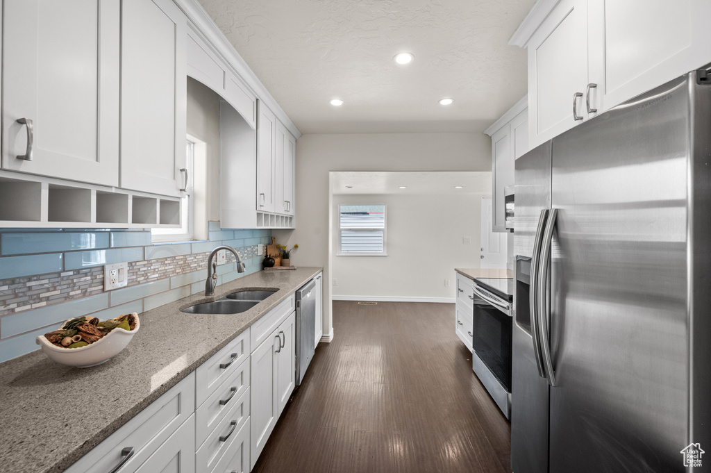 Kitchen featuring appliances with stainless steel finishes, a sink, baseboards, backsplash, and white cabinetry